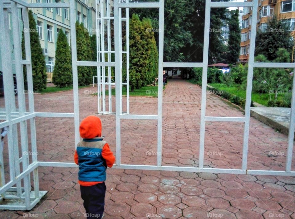 малыш смотрит сквозь ограждение the kid looks through the fence