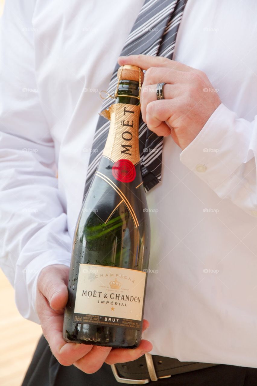 Married man in a crisp white shirt holding a champagne bottle, ready to pop the cork