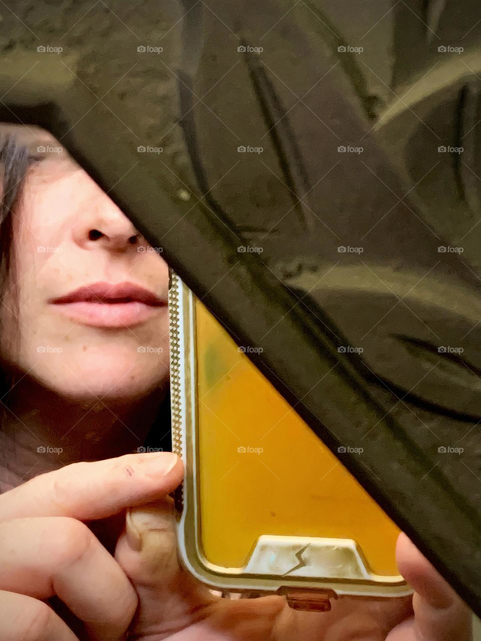 Selfie in a floral frame mirror seeing the woman’s face in an angle hiding a small part of the face and showing the phone taking the picture close-up.