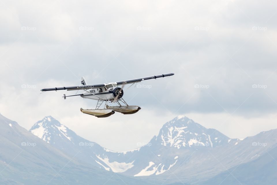 Seaplane getting ready to land. Seaplane getting ready to land. Mountain peaks on the background. Clouds in the sky. Seaplane is white and blue. Alaska