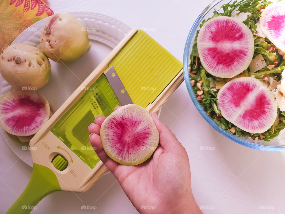 Hot pink watermelon radishes being sliced on a lime green mandoline slicer for a salad.