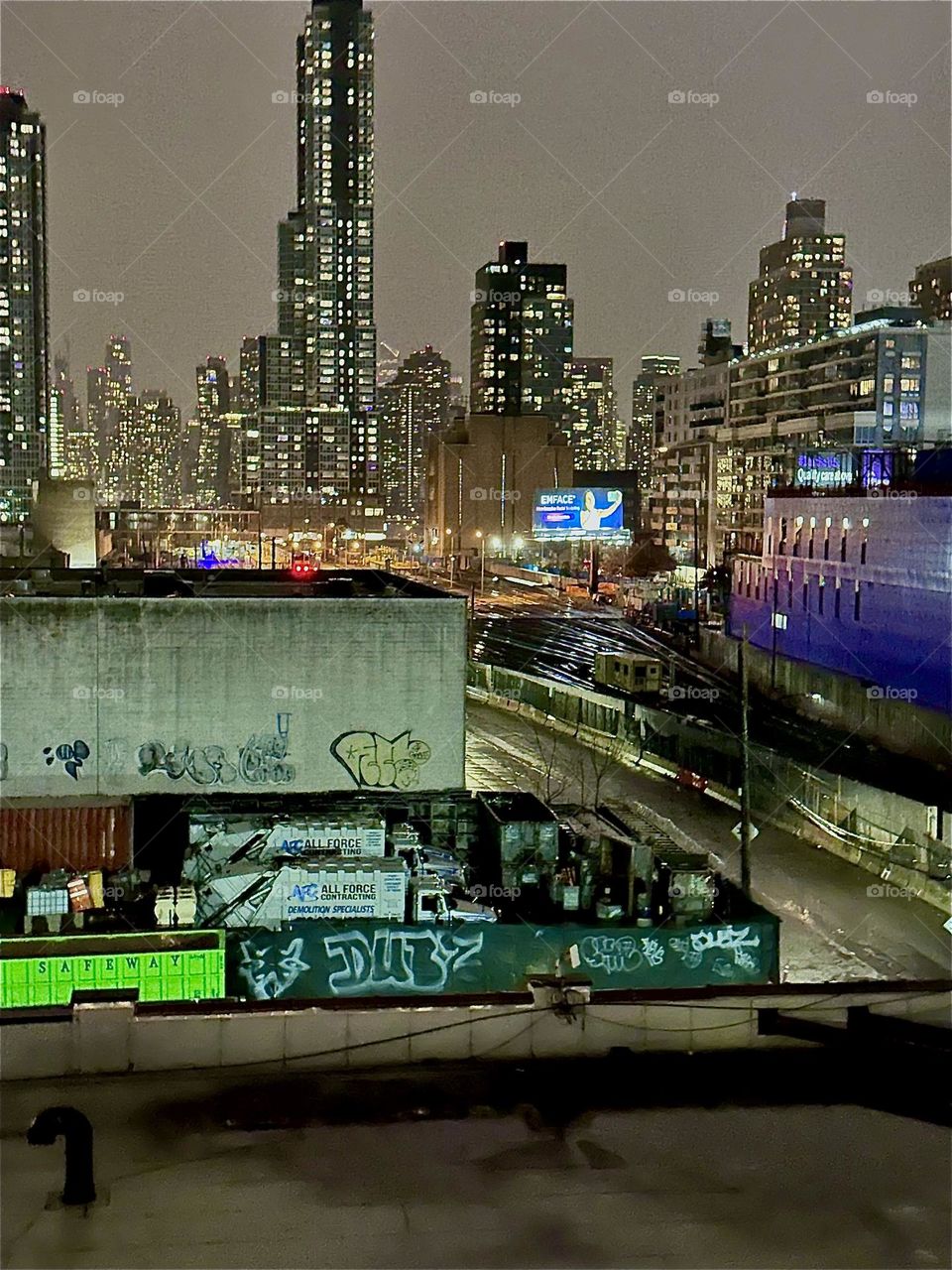 This is a nighttime impression from the stairs of the “Pulaski Bridge” in LIC, Queens overlooking adjacent buildings, the train tracks of the “Long Island Railroad” and the combined skyline of LIC and “Manhattan”. 2023. Hypnotic Productions