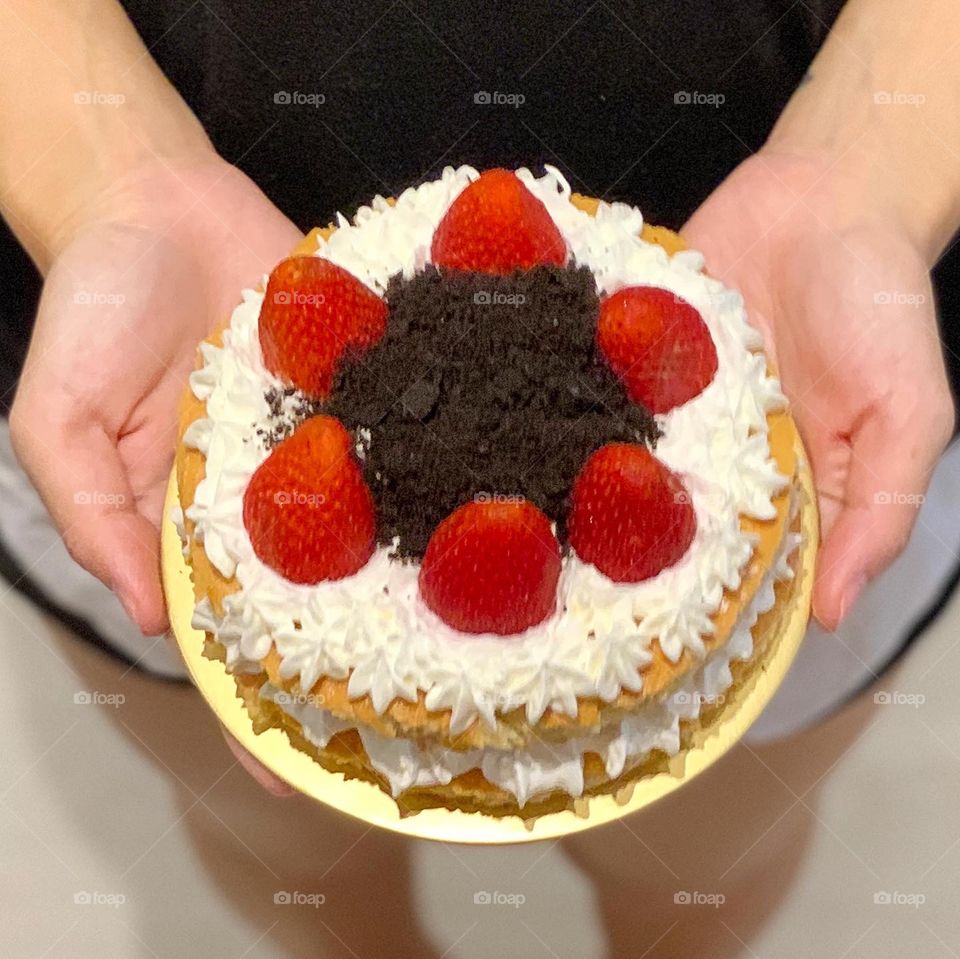 Lady holding on to 6 inch 2 layered Strawberry shortcake that looks fresh and delicious 