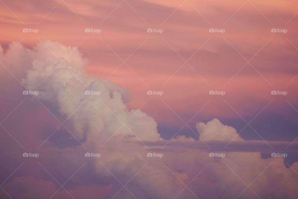 A thin stratus cloud in front of expanding cumulonimbus clouds against a beautifully painted sky 