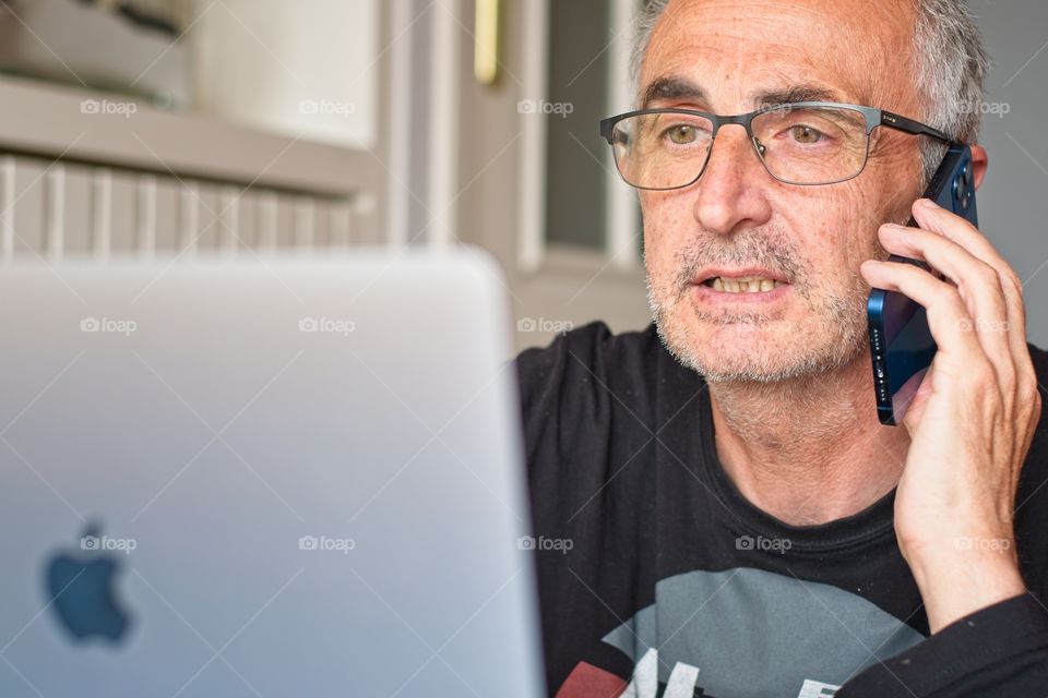 Man working on his Apple MacBook at home and talking on the phone