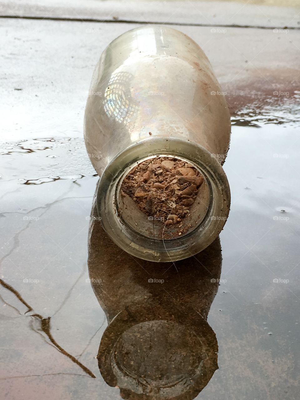 Antique milk bottle in the rain on its side filled with seashells and sand as dug up, reflecting in the rainwater