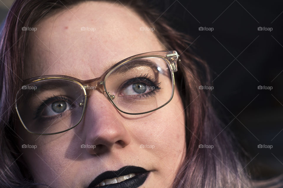 A young woman with purple hair and black lipstick looks at the sun with beautiful green eyes