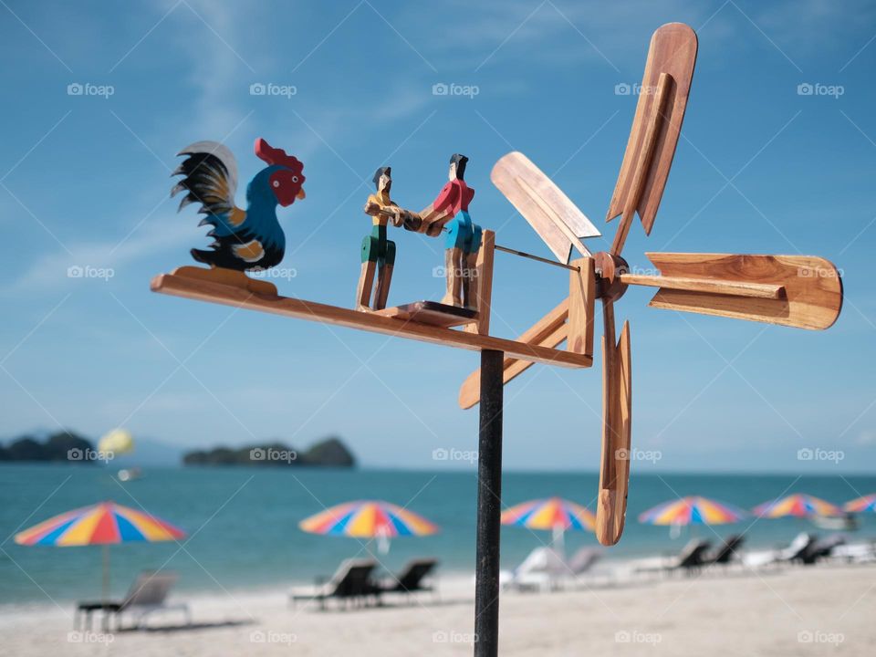 Close-up of a cute windmill on the beach against rows of colorfull umbrellas in Langkawi, Malaysia