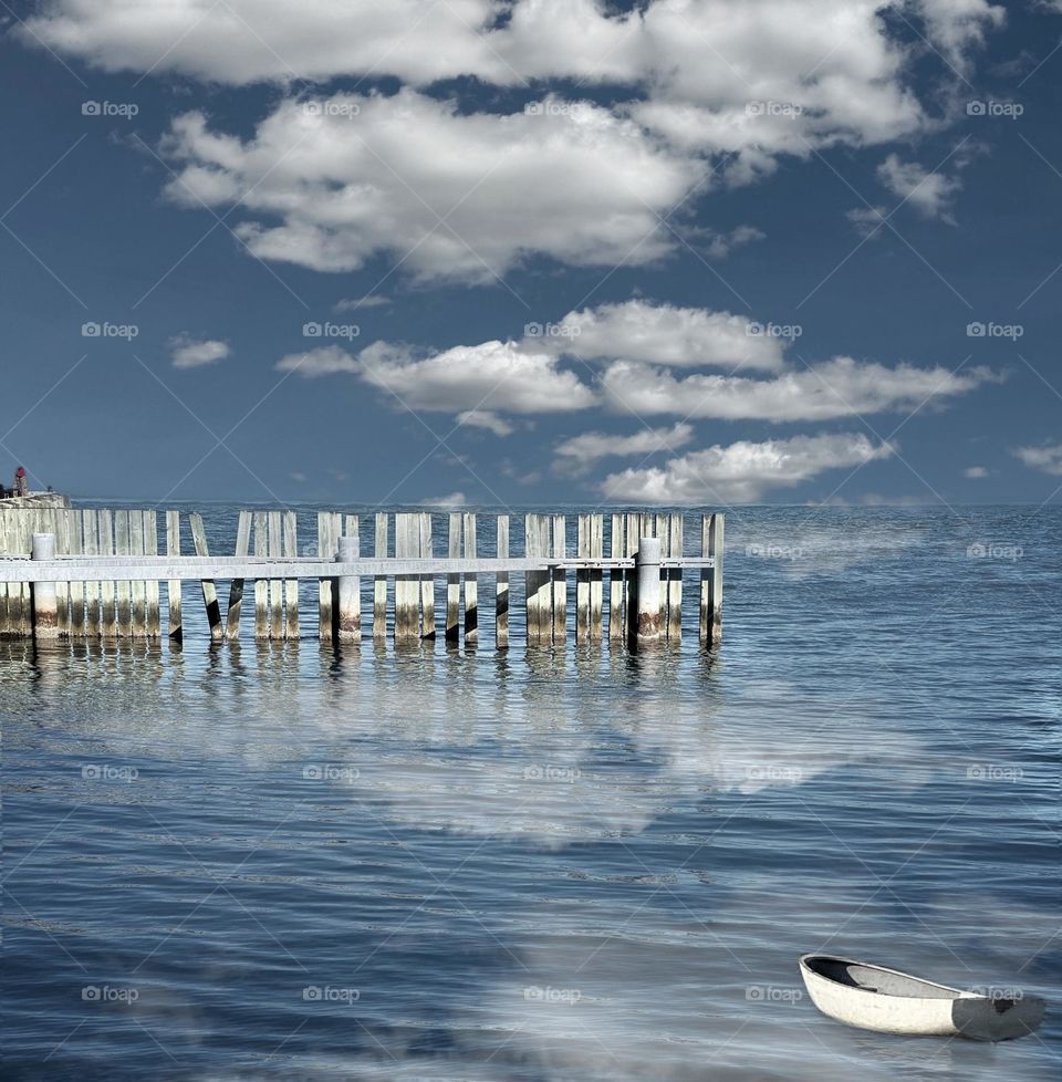 A fence and small boat on the Atlantic coastline with clouds in the sky and reflections of clouds in the water 