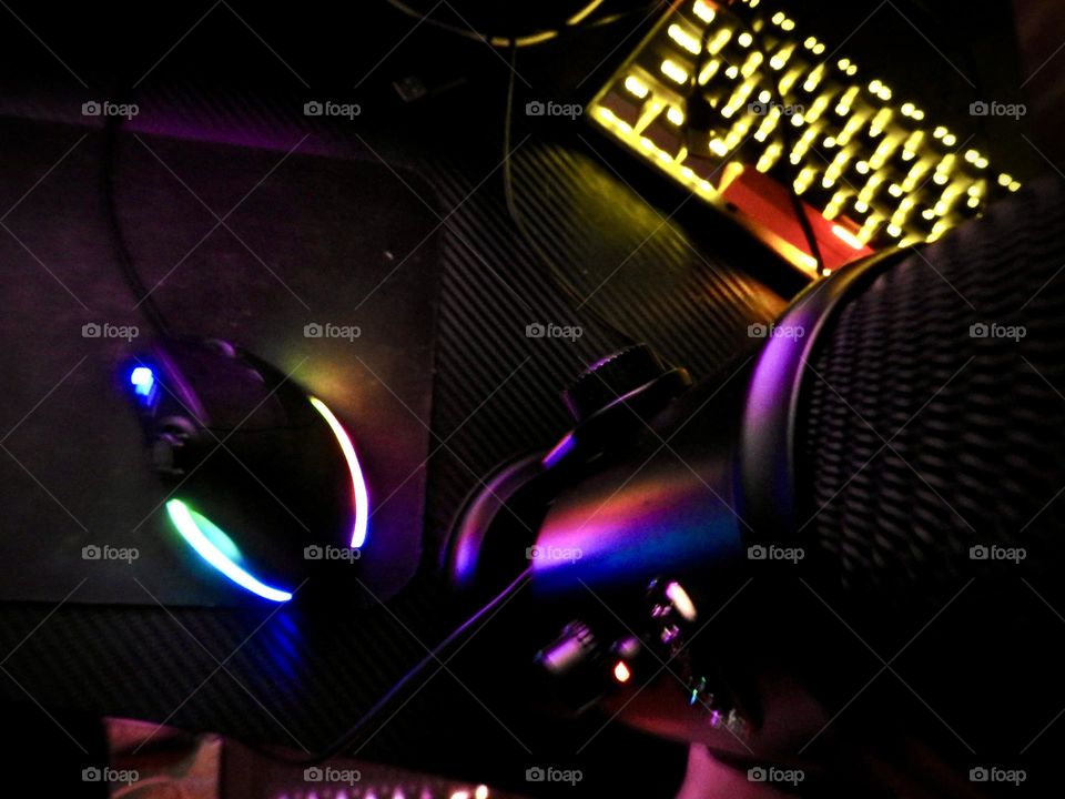 Gaming set showing accessories in a dark room enhancing the beautiful effect with the illuminating of different color lighting through them on a gaming desk.