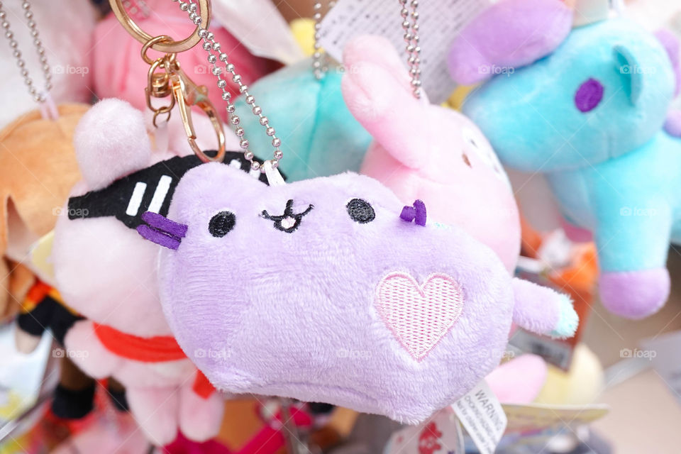 Souvenir plush dolls. Adorable stuffed animal toy keychains on display on sales, in Japan walking street market. Selective focus on the purple cat with a pink heart