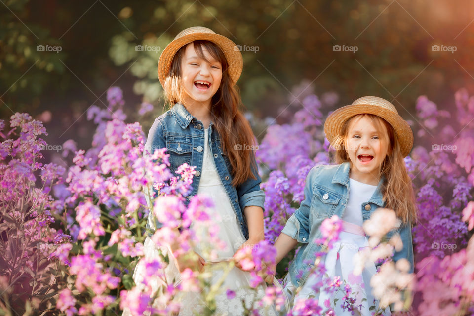 Little sisters in a blossom meadow at sunset 