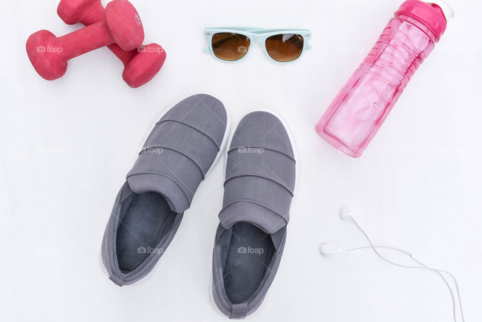 Flat lay of workout accessories consisting of dumbells, water bottle, earbuds, sneakers and sunglasses