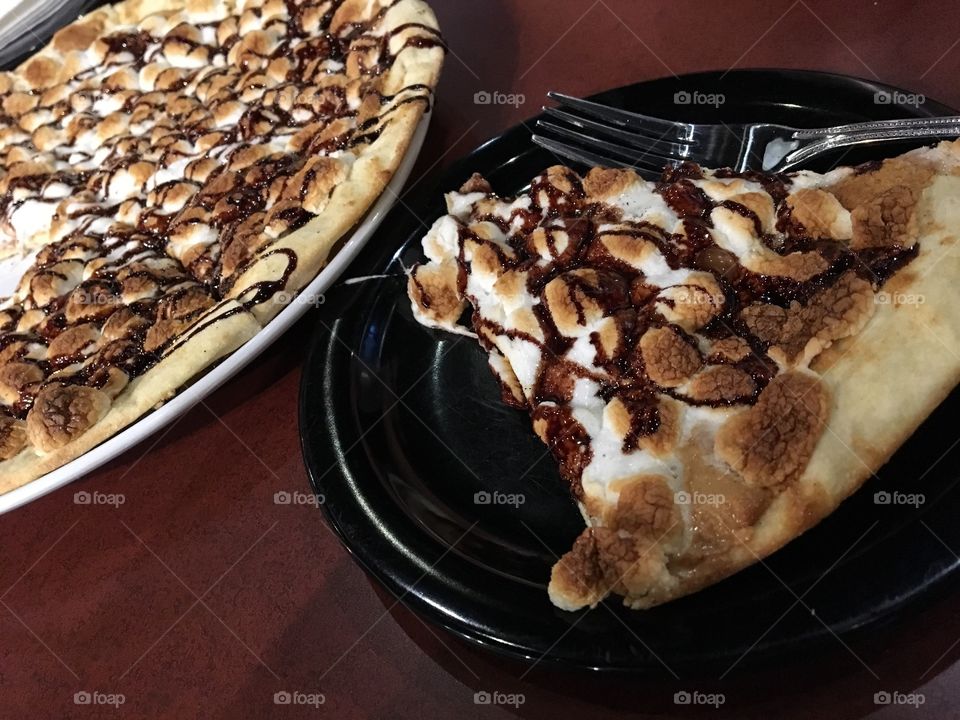 Pizza covered with peanut butter and topped with chocolate drizzle, graham cracker crumbles and marshmallows 