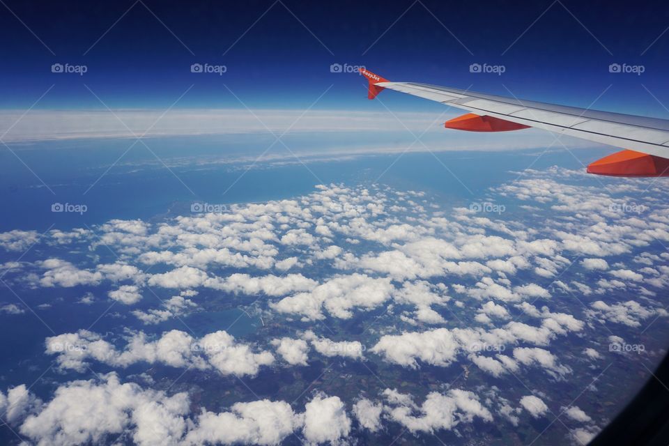 Window view from an Easy Jet Aeroplane.. puffy white clouds with a bright blue sky and glimpses of land below ..