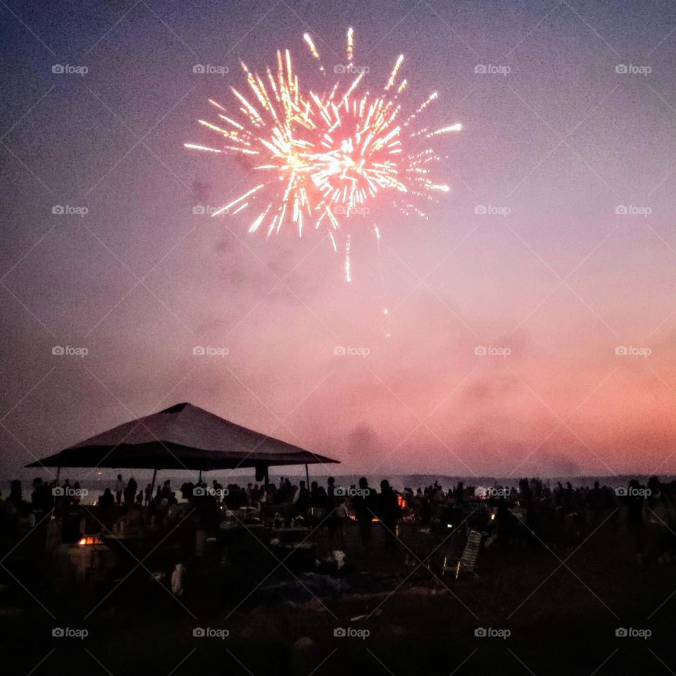 A dazzling fireworks display on a sandy beach, on the Puget sound, with cabana tents and a ton of spectators on the 4th of July