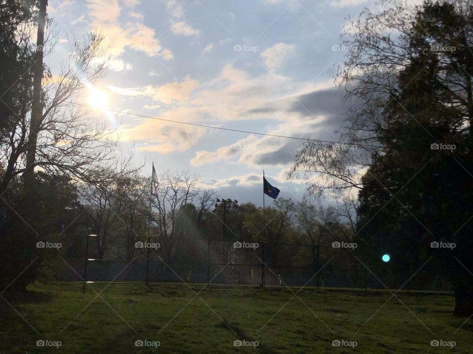 Beam of light coming from a bright spring sun with fluffy clouds and the silhouette of a flag pole 