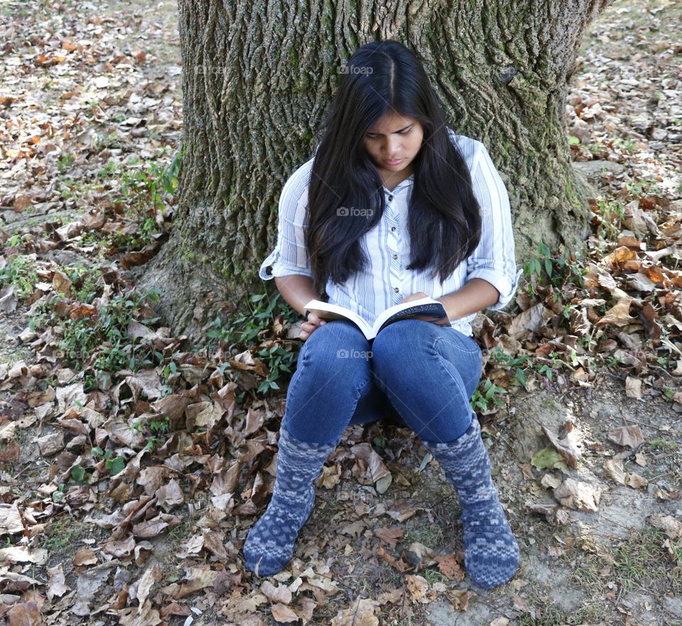 Girl sitting outside under a tree reading a book 