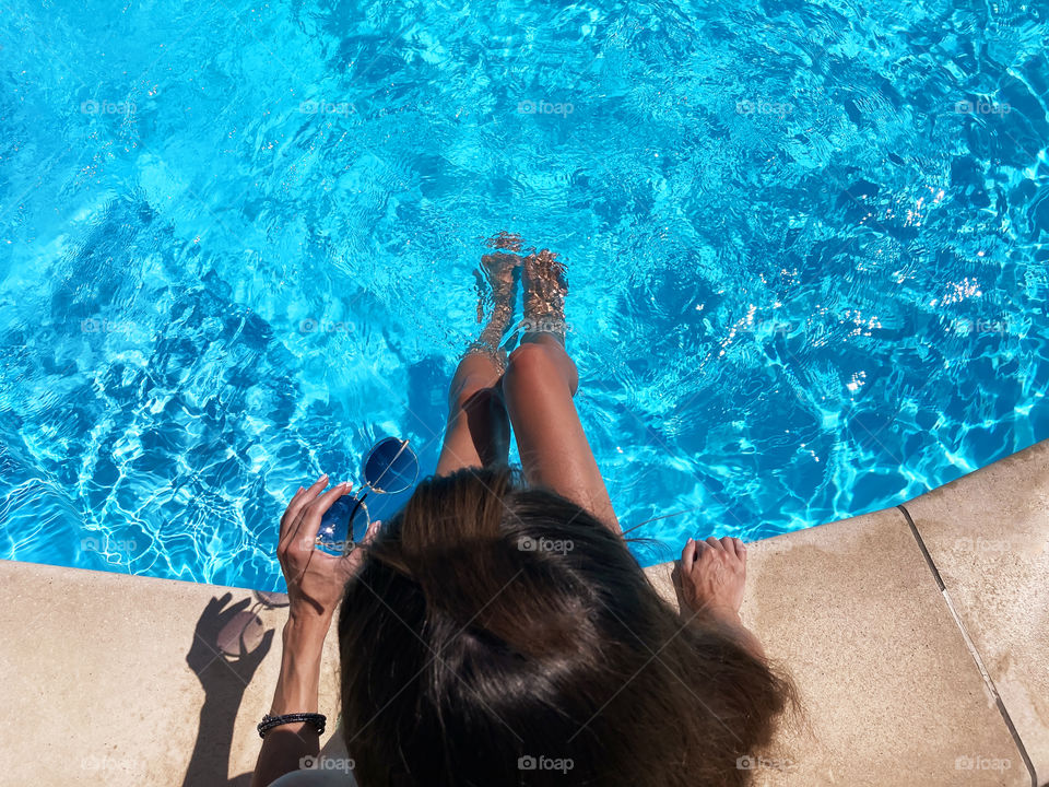 Young woman with long hair and sunglasses in hand at the swimming pool 