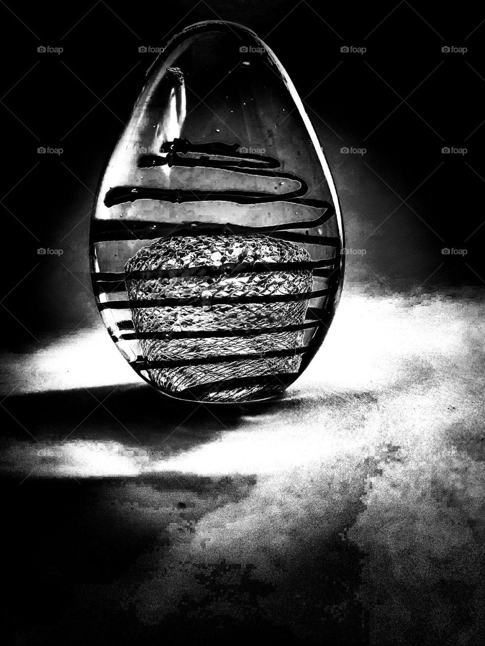 Black and white still life of an egg shaped glass art with a swirl inside and a mesh inside.