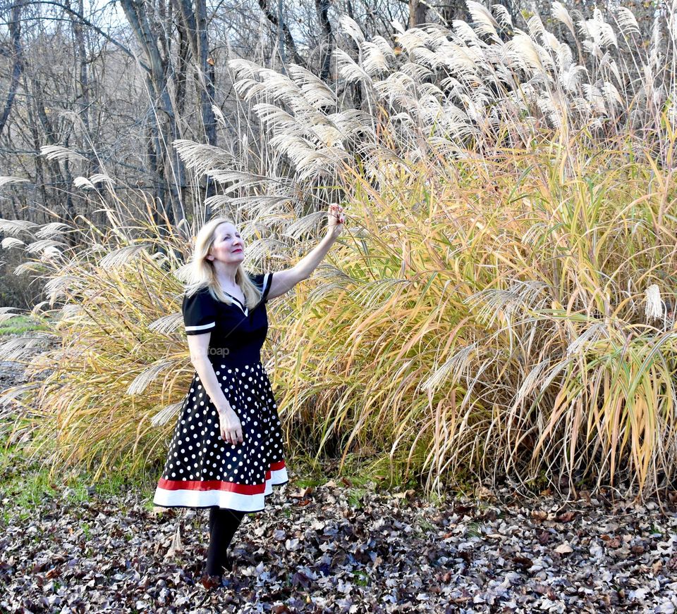 Woman in a black, red, and white dress beside some tall plants