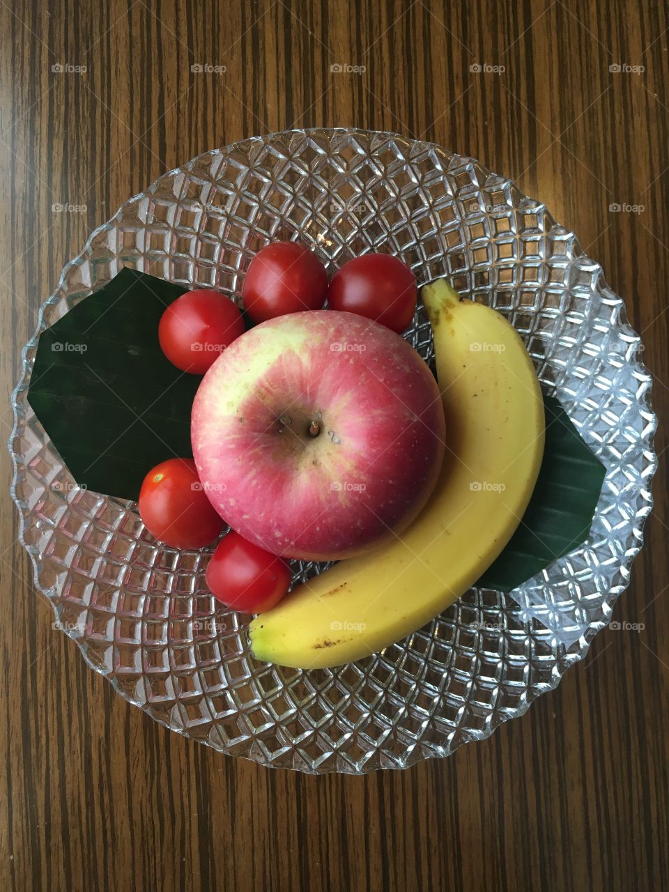 Fresh banana, apple and tomatoes on the transparent plate