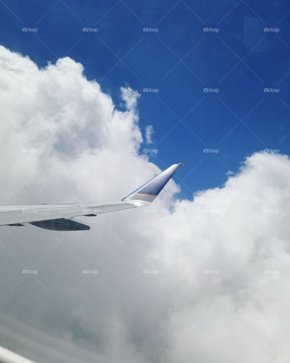 The wing of a plane up in the sky with blue skies and fluffy white clouds