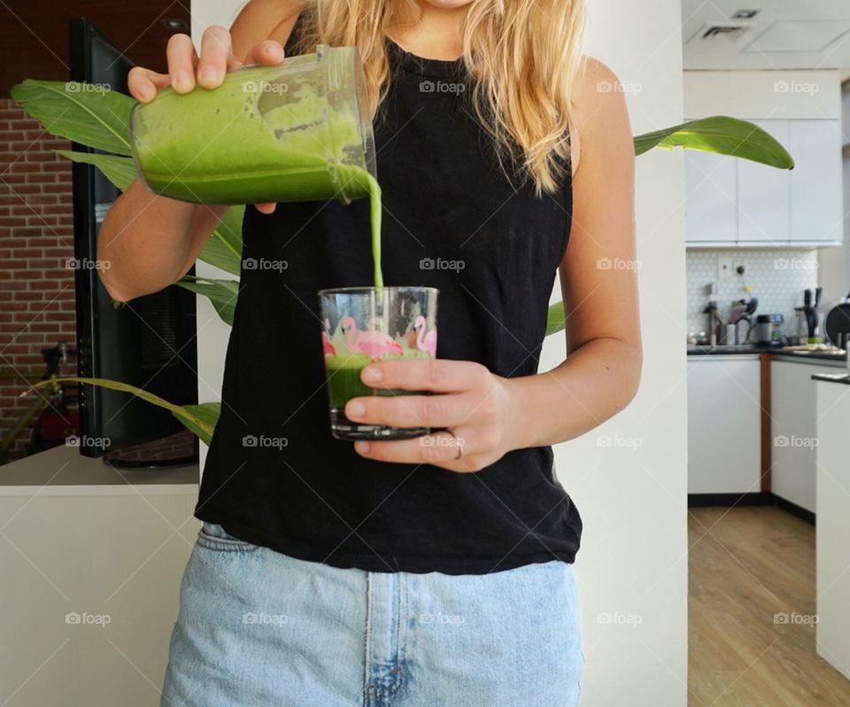 A woman pouring green juice in a glass