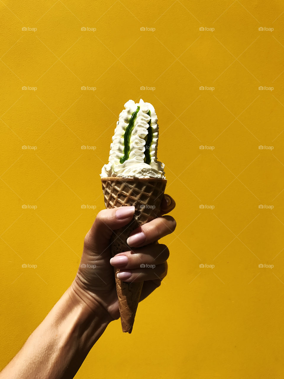 Female hand holding an ice cream cone on yellow background 
