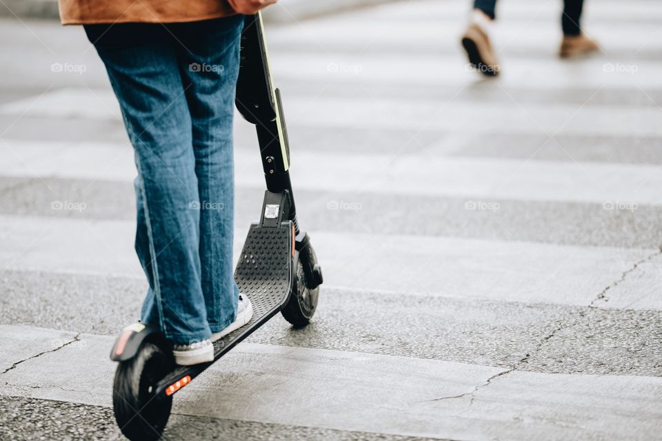 milenial crosses a crosswalk on a scooter