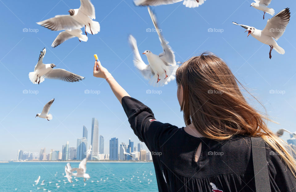 Young woman feeding the seagulls at the beach in summer