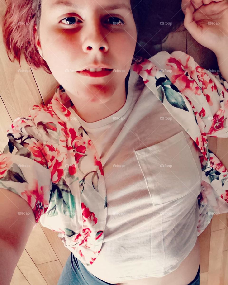 A girl with short hair lays on a wood floor in a flowered robe. She has short bred hair