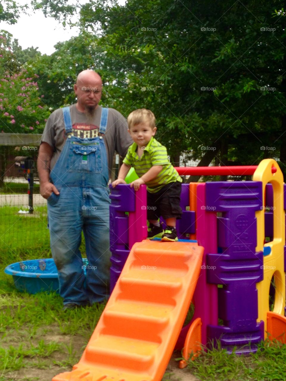 Pawpaw helping grandson playing on a plastic toys. Pawpaw wearing  denim overalls