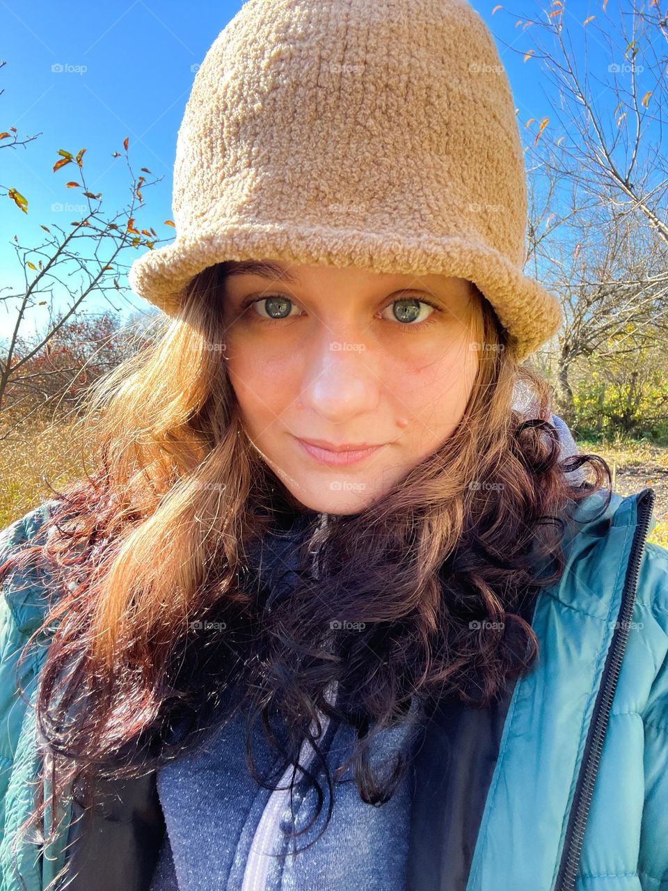 Funny and cozy portrait of girl in a knitted hat with blue eyes and curly hair under the autumn sunshine