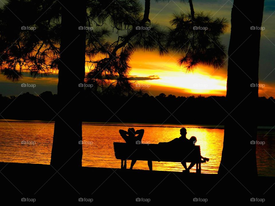 Silhouette of people sitting on bench near the lake