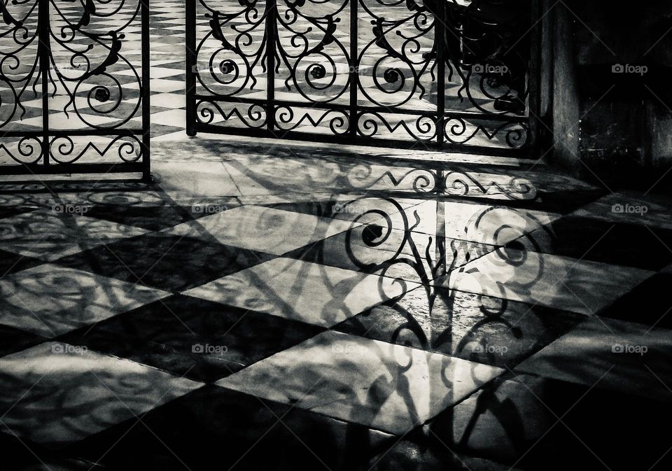 Shadow of an ornate cast iron gate on a checkered tile floor