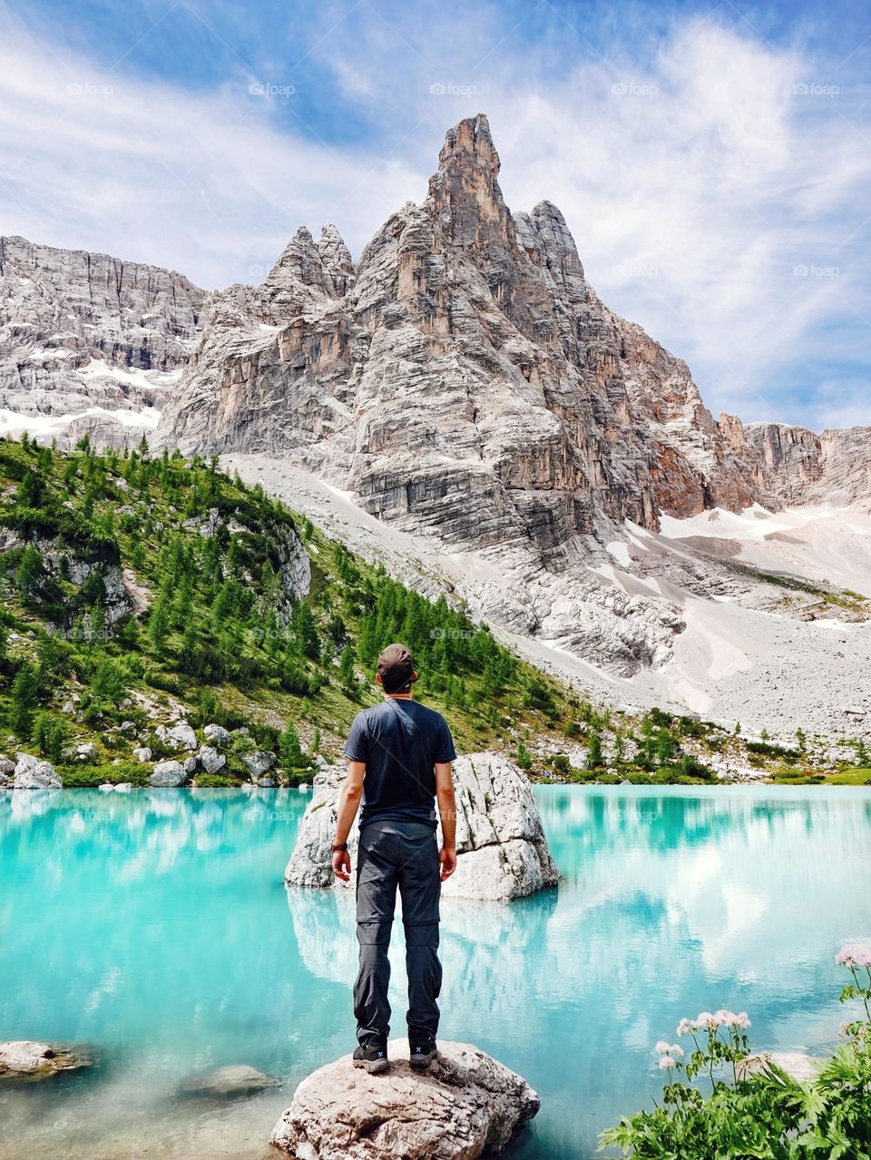 Rear view of man stading on shore of spectacular emerald lake under rocky mountain at Lake Sorapis in Italy