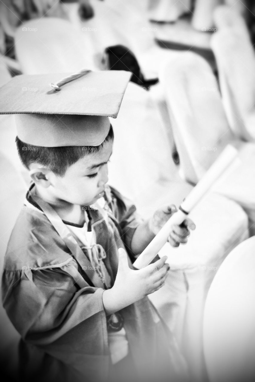 Boy wearing graduation gown holding certificate