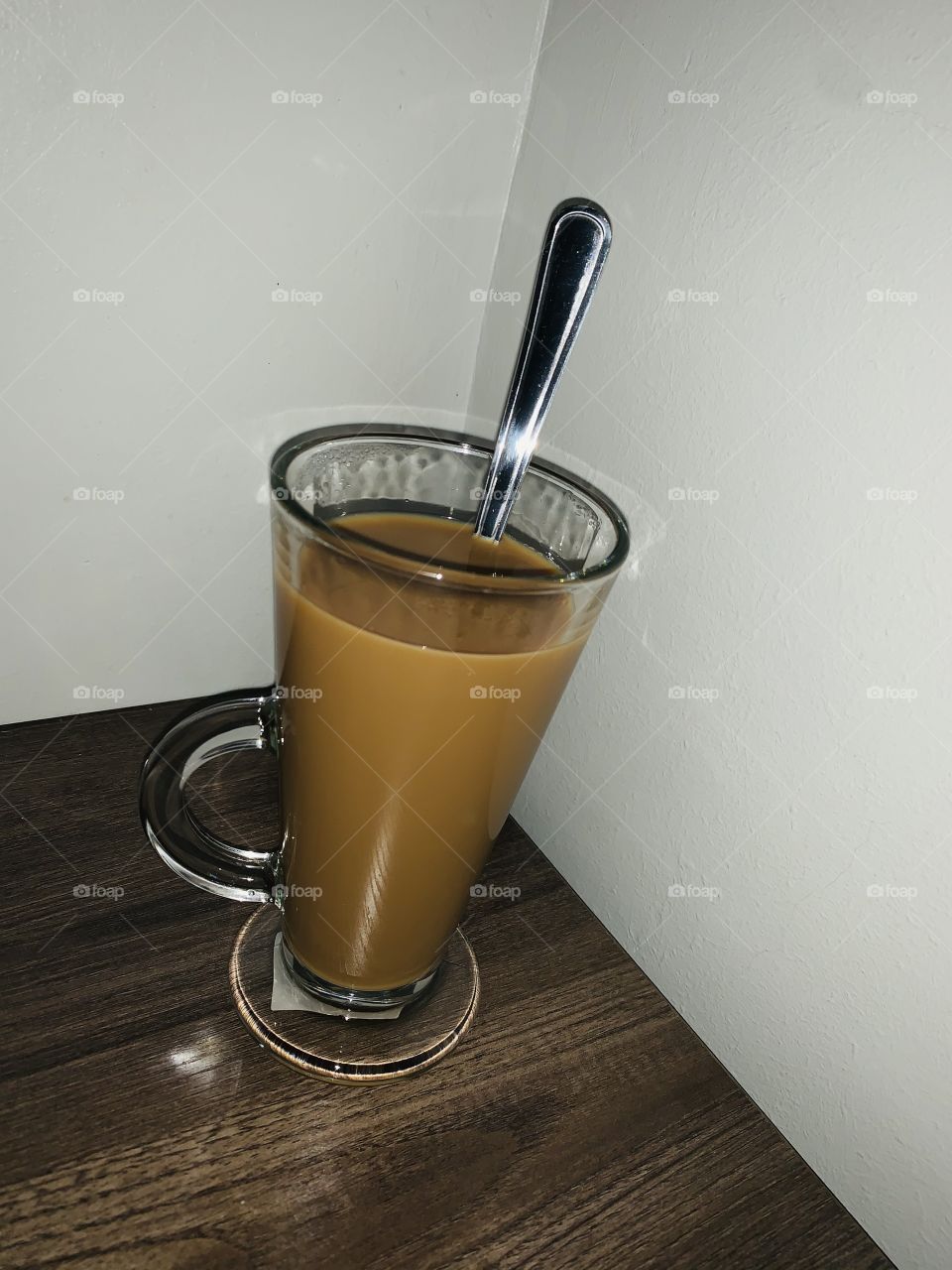 A glass of homemade coffee on a table with a long silver teaspoon.