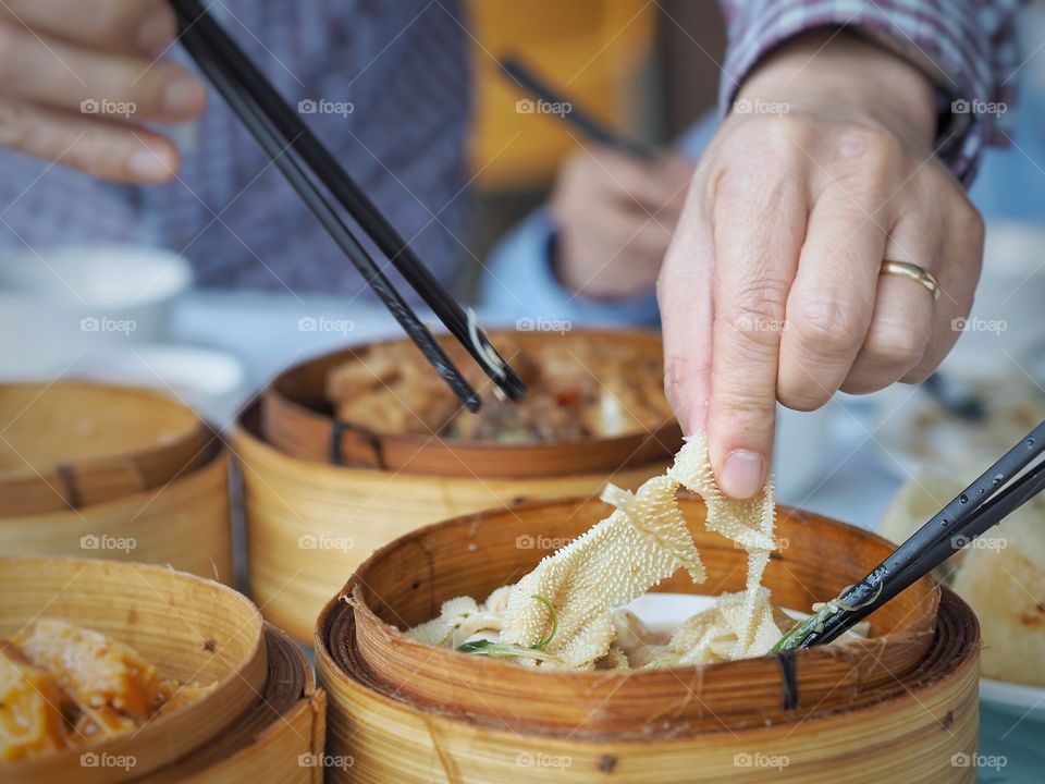 Tripe braised with chilli and shallots. Finger and chopsticks sampling the tripe. A popular food item in a yum cha or dim sum line up. The dish is kept warm inside a bamboo steamer.