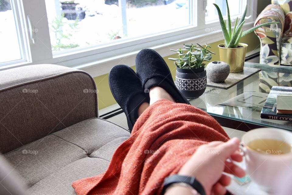 Woman having tea while resting on couch enjoying view of the backyard out of the window