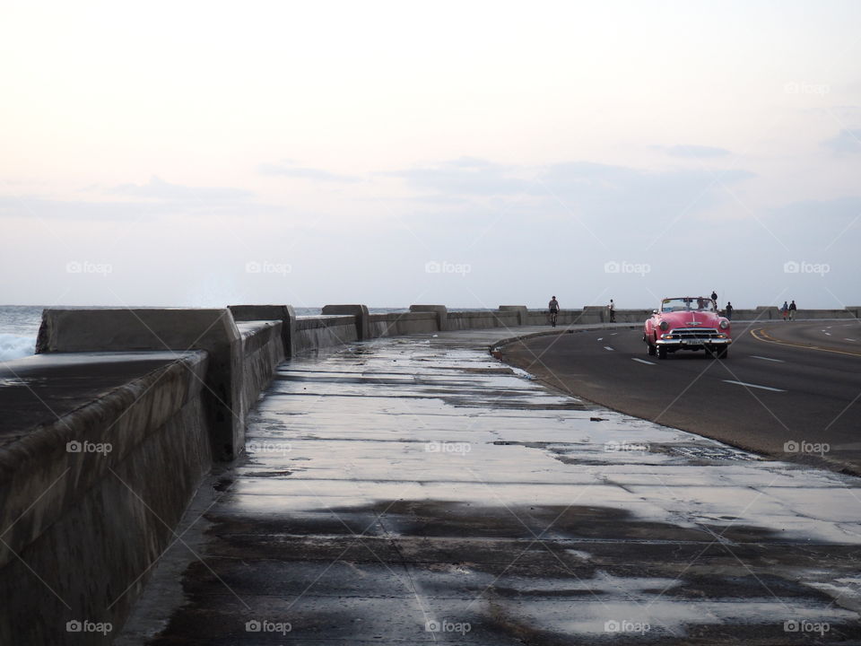 Pink oldtimer driving on the coast side of Havana, Cuba during sunset on a sunny day.