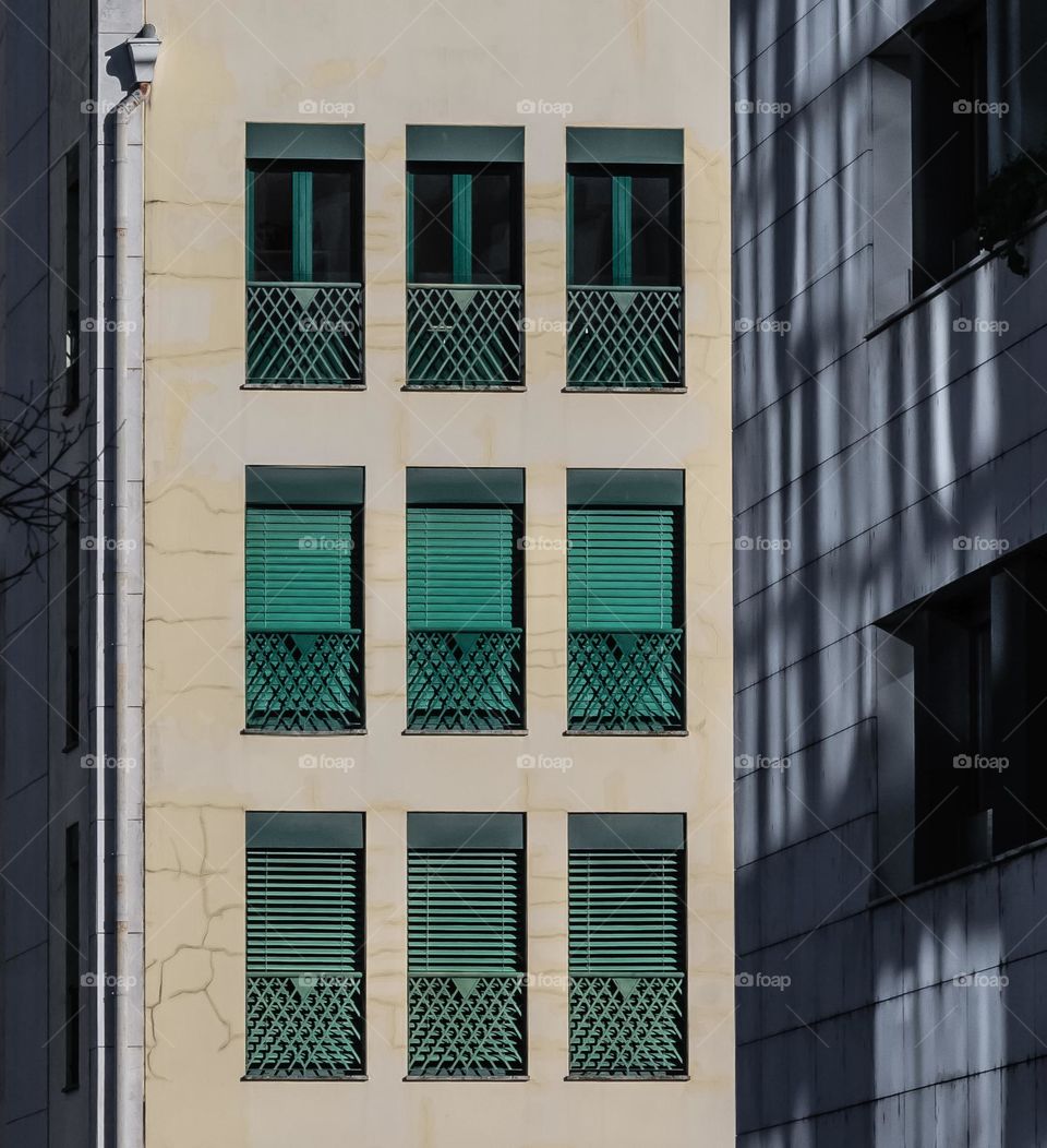 Rectangular green shutter adorn this apartment building, with rectangular shadows on the adjacent wall 