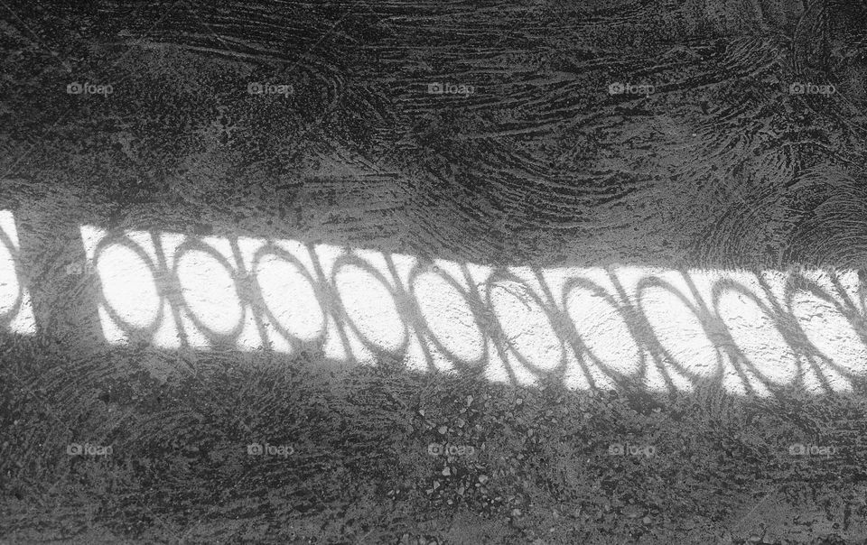 The shadow of the fence on the concrete sidewalk.  Representation of geometric shapes: circle and rectangle