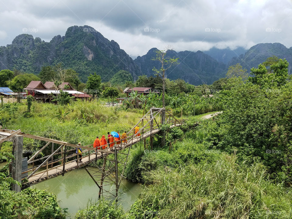 monks walk across a bridge in Laos
