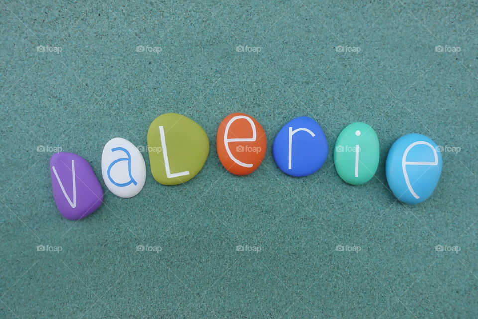 Valerie, feminine given name composed with multi colored sea stones over green sand