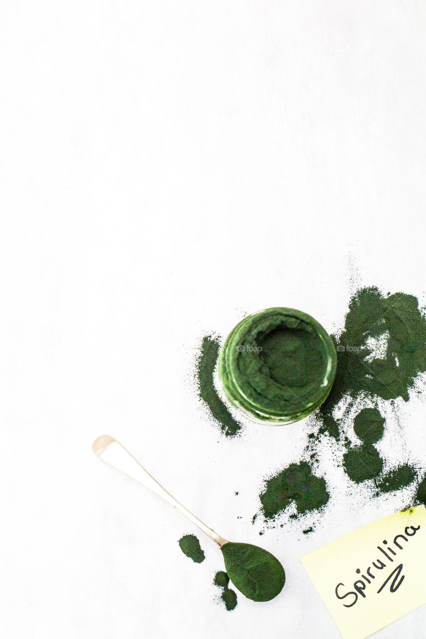 Product spirulina green powder on white background - image from top with powder and note