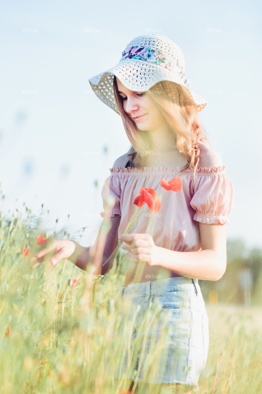 Beautieful young girl in the field of wild flowers. Teenage girl picking the spring flowers in the meadow wearing hat and summer clothes. Spending time close to nature
