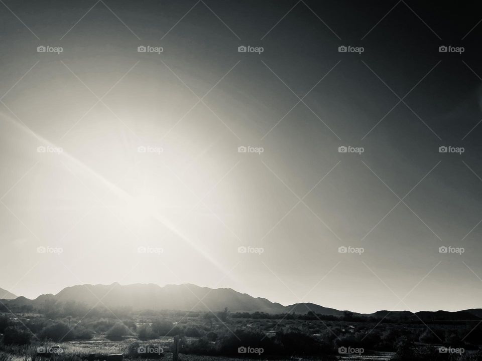 A black and white photo of the sun above a mountain range. 
