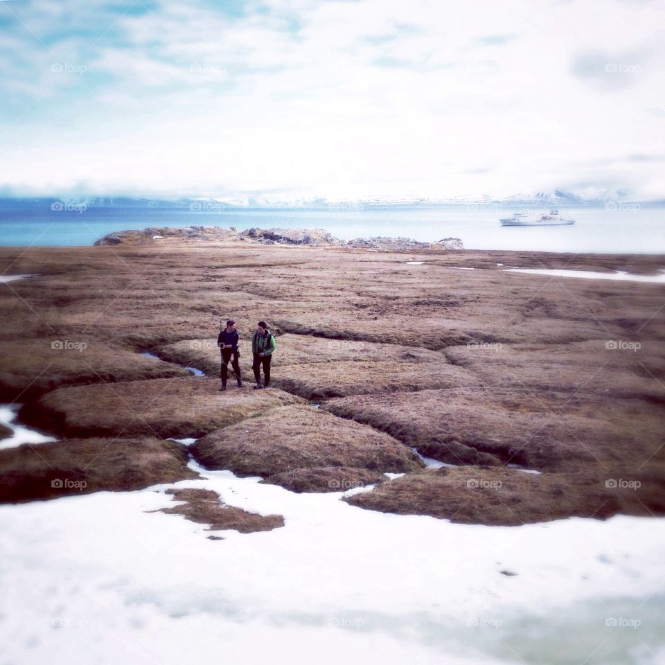 Two people hike along the tundra of Spitsbergen, Svalbard.